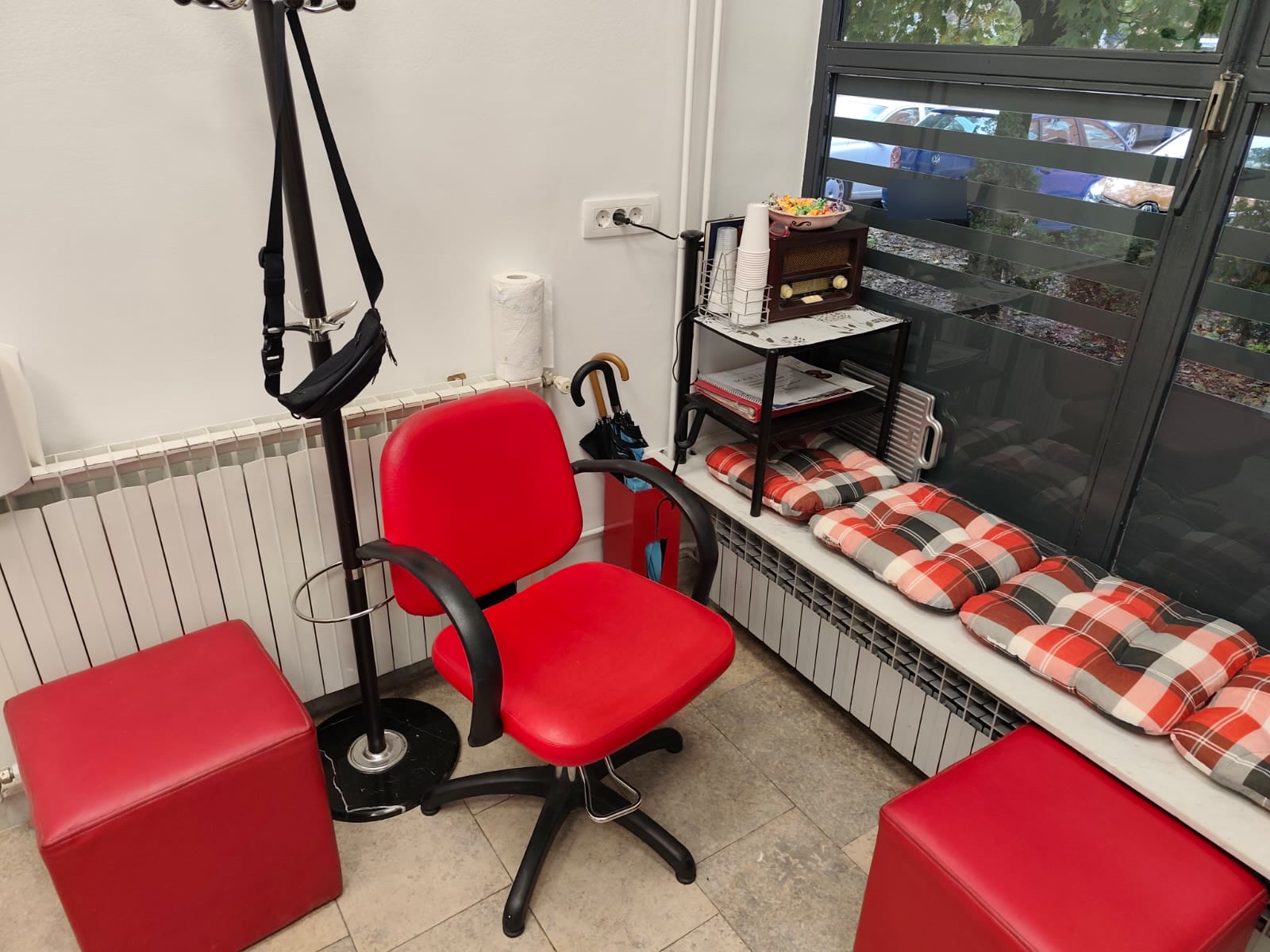 Kutak za čekanje u frizerskom salonu Martina: crvena frizerska stolica, crveni tabureti, karirani jastuci i stari radio uz prozor.
